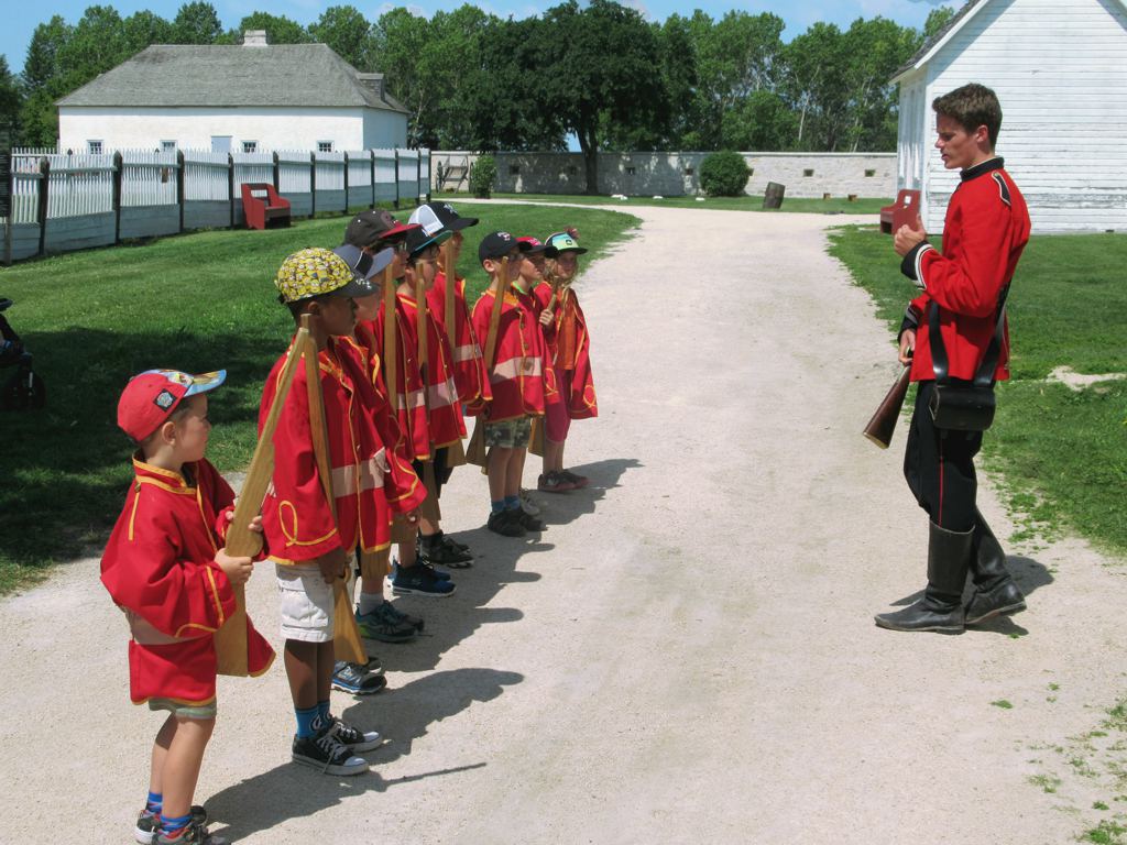 Children dressed in Canadian mountie costumes stand in front of a historical interpreter, also dressed as a Mountie, at Lower Fort Garry.
