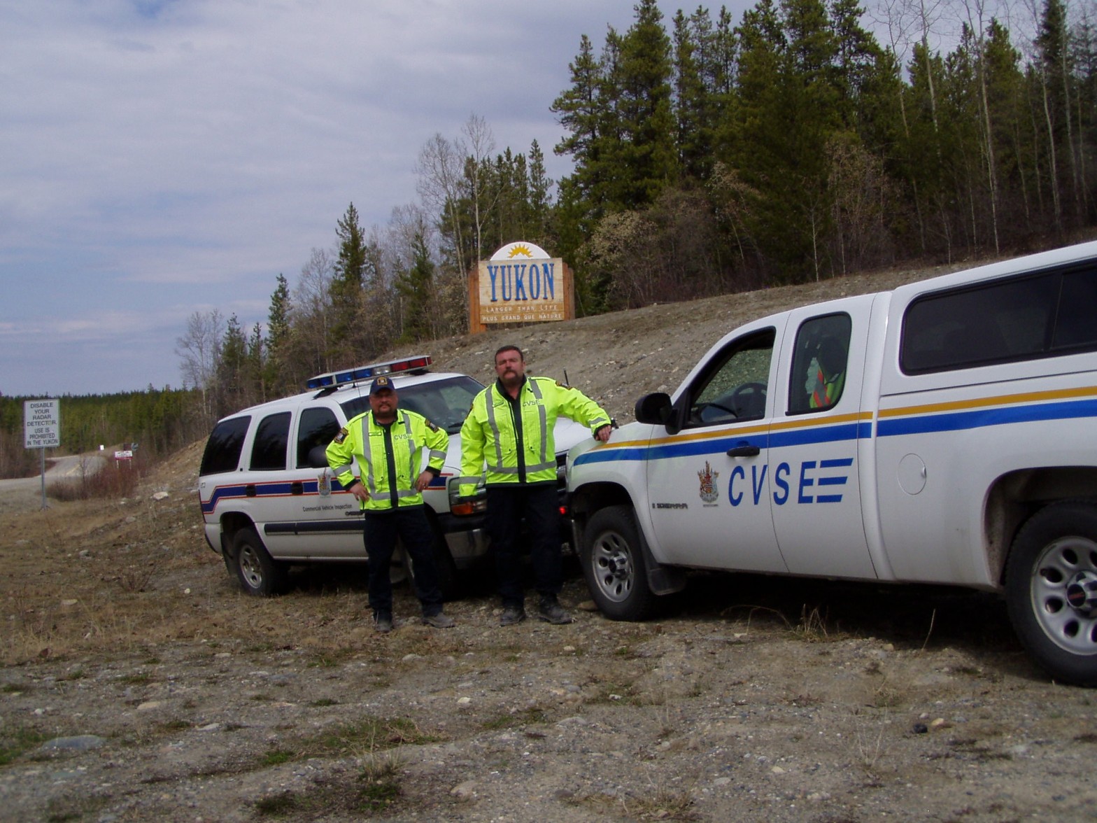 Skeena District Commercial Vehicle and Safety Enforcement (CVSE) officers participated in a multiagency commercial vehicle safety check in the Yukon, just over the BC border. They stand in reflective gear in front of two official trucks parked in front of the Yukon Territory border sign.