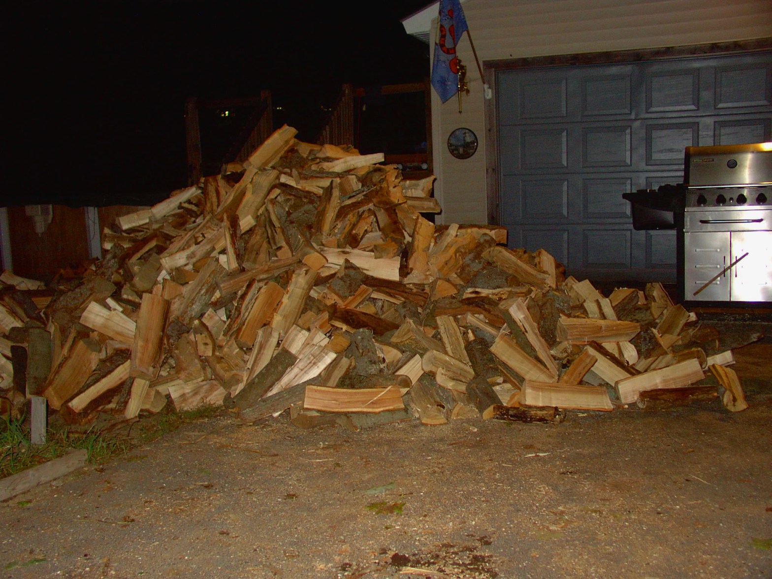 large pile of split firewood beside a garage and propane grill